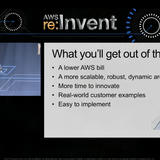 AWS re:Invent 2014 conference slide showing Constantin in a light blue shirt standing on stage. The slide title reads “What you’ll get out of this session” with five bullet points: A lower AWS bill, A more scalable, robust, dynamic architecture, More time to innovate, Real-world customer examples, and Easy to implement. A mountain with a flag icon appears in the bottom right corner of the slide.