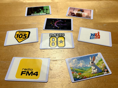 Eight white NFC cards arranged on a wooden surface, displaying various radio station and music service logos: Groove Salad, Chillhop, Beat Blender, Radio 105 Network, Radio 80, NRJ Made in France, Radio FM4, and a cute Easter bunny card saying 'Ruhe… (alles aus)' with a rabbit in a meadow.