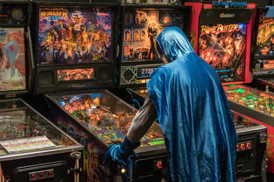 A man in a Batman costume, playing Pinball